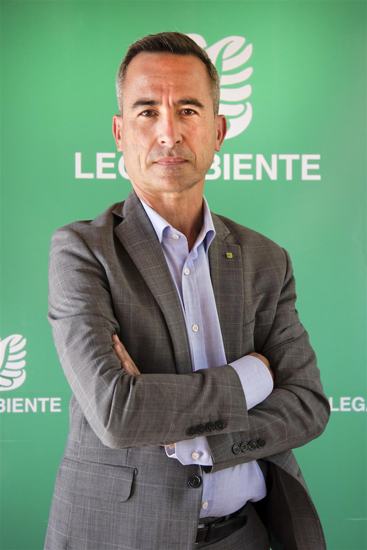 Stefano Ciafani in giacca e camicia, con le braccia incrociate, davanti a uno sfondo verde con la scritta "Legambiente" e il logo 