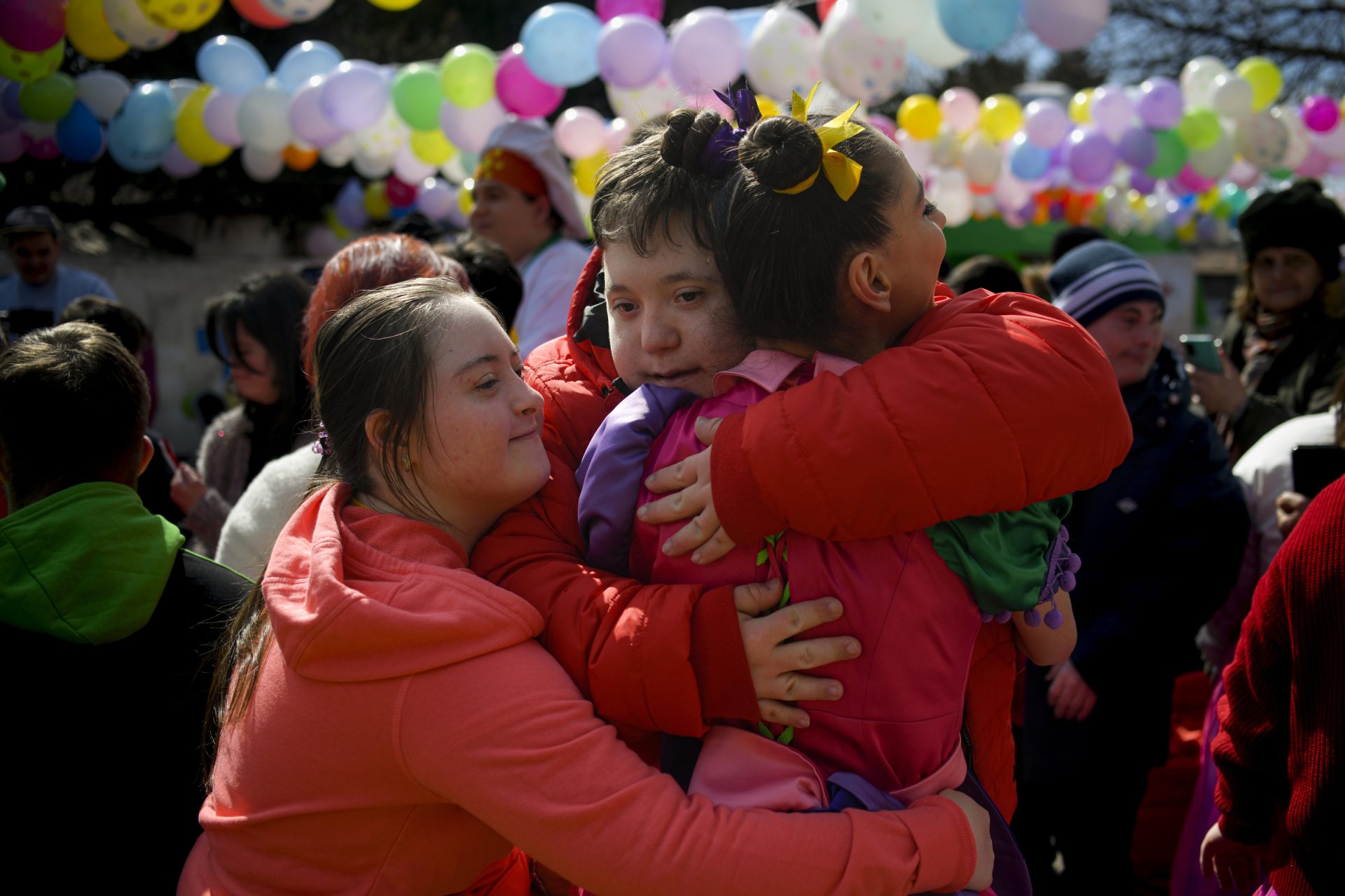 Tre ragazzi con disabilità intellettiva si abbracciano durante una manifestazione per il World Down Syndrome Day
