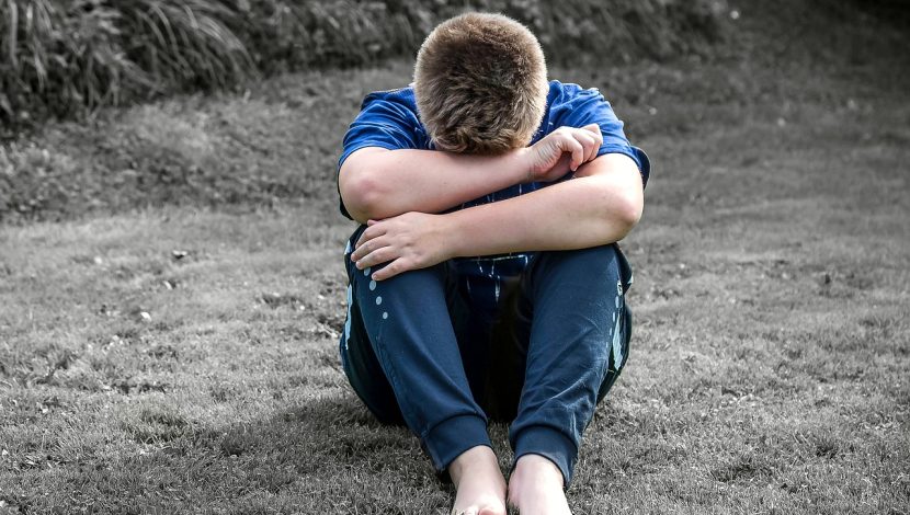 Ragazzo a colori, seduto sull'erba in bianco e nero, con la testa tra le braccia incrociate