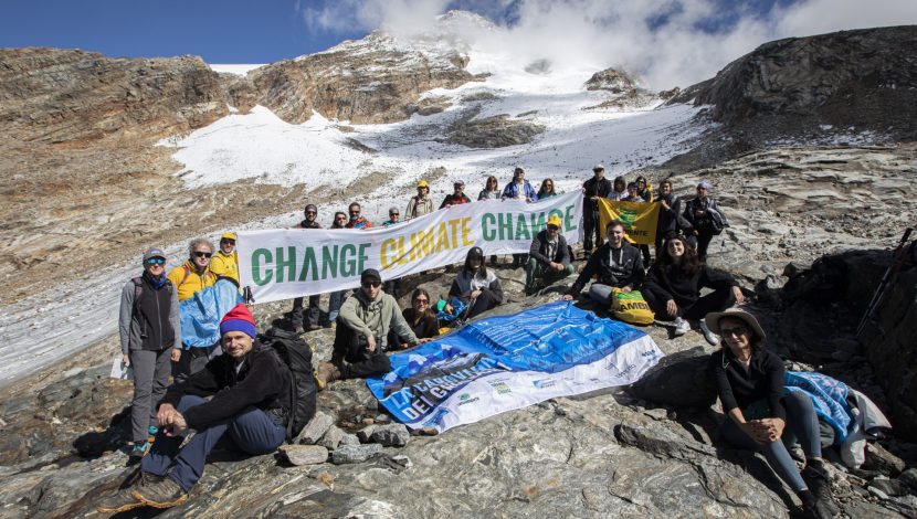 Gruppo di persone in montagna, tengono in mano un cartello con scritto "Change climate change"