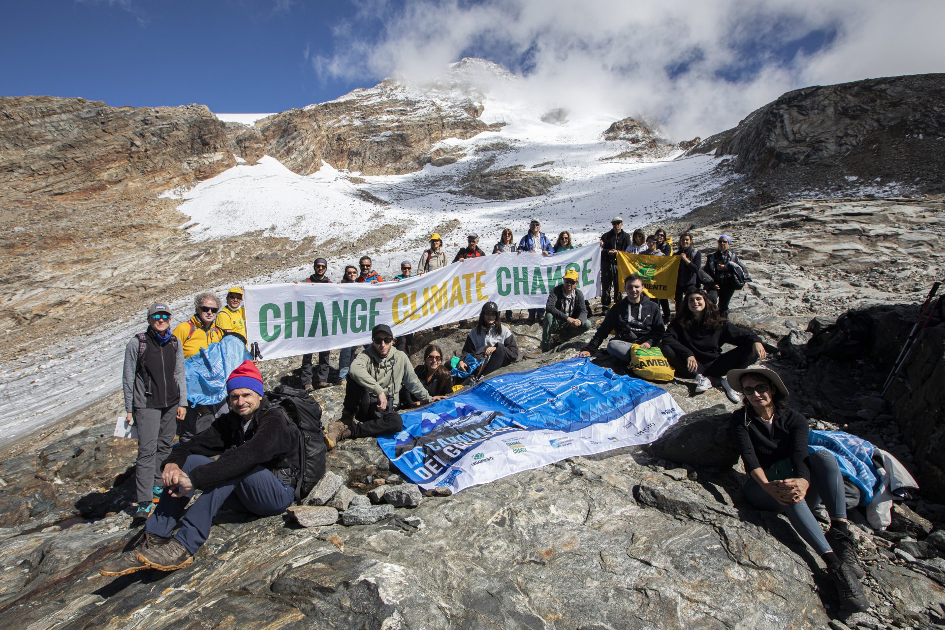 Gruppo di persone in montagna, tengono in mano un cartello con scritto "Change climate change"
