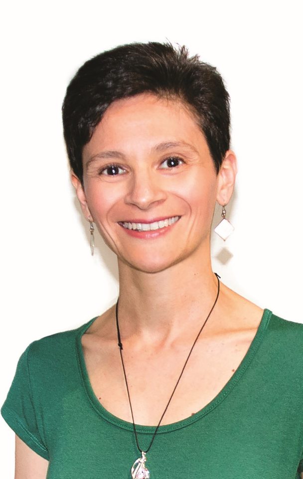 Elena Moretti su sfondo bianco. Ha i capelli corti neri e una maglietta verde, con una collana e orecchini
