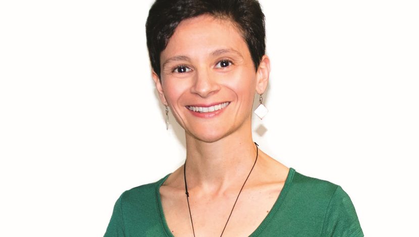 Elena Moretti su sfondo bianco. Ha i capelli corti neri e una maglietta verde, con una collana e orecchini