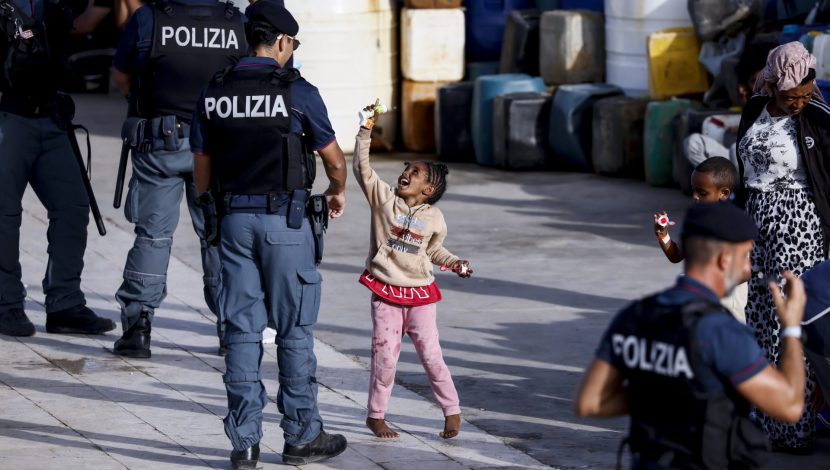 Bambina al centro dell'inquadratura, rivolta verso un'agente di polizia di spalle