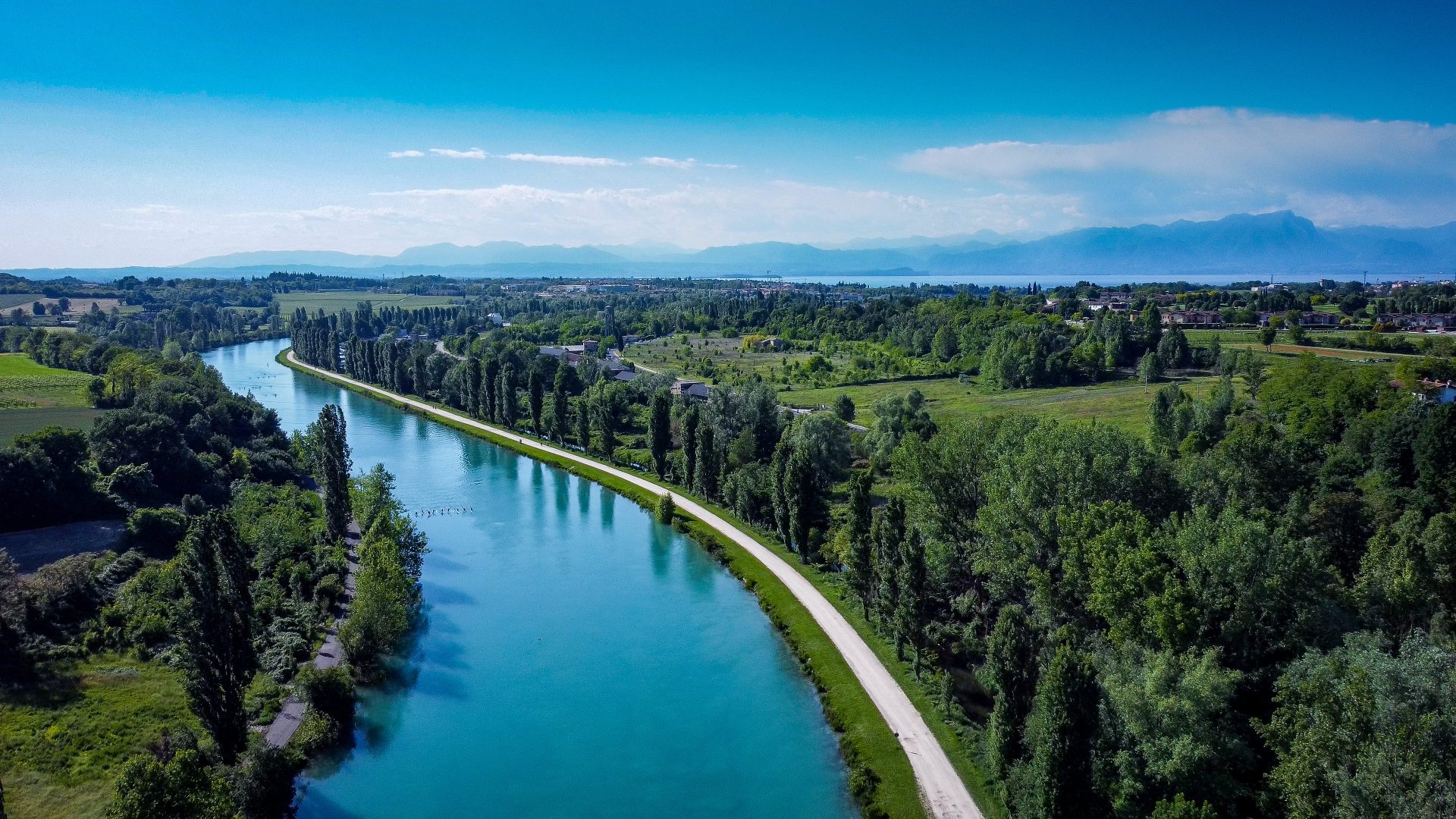 Sulla sinistra, un'ansa del Mincio, sul lungofiume alberi e oltre campagna. Sullo sfondo, colline