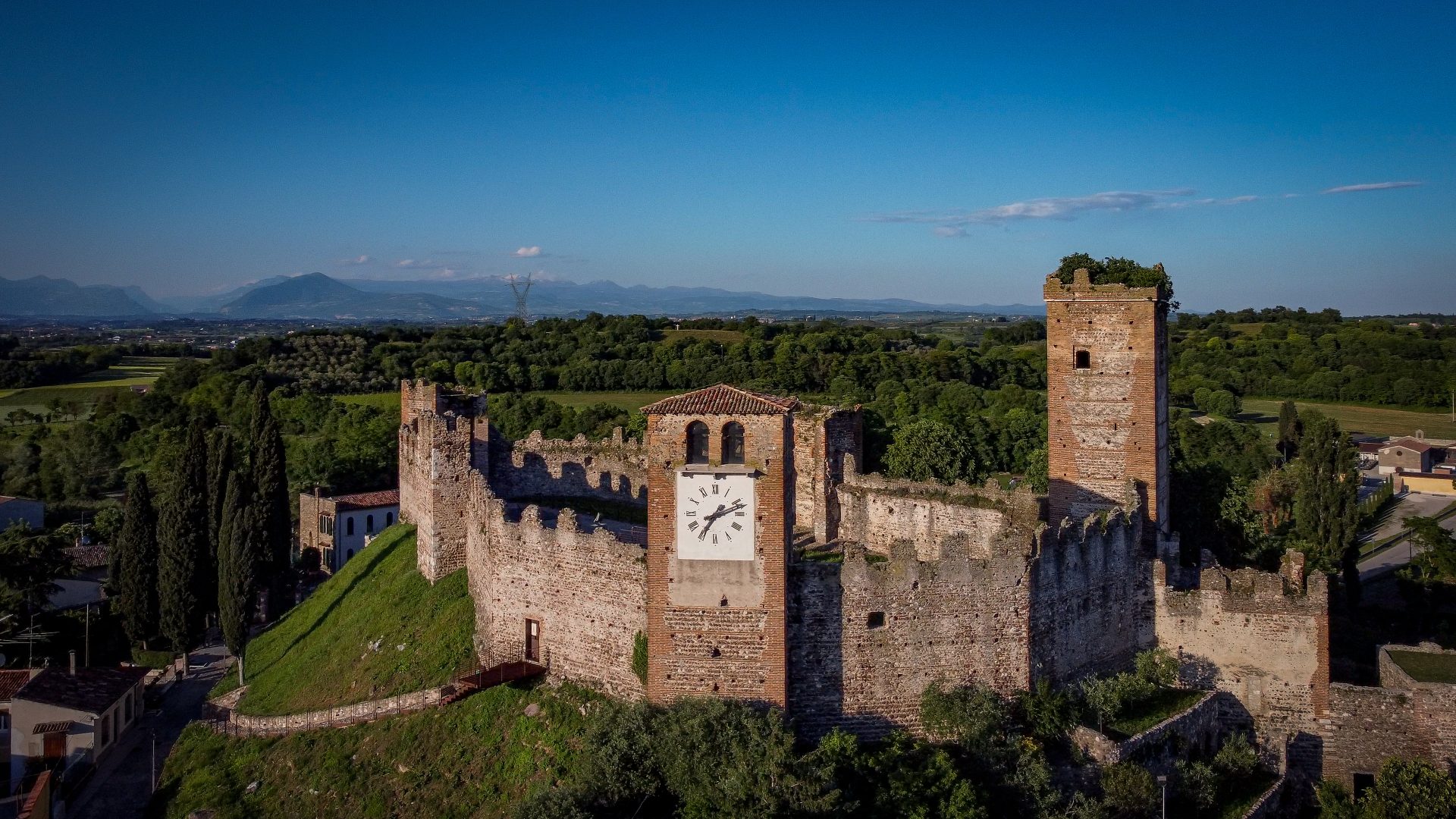 Veduta aerea delle mura di un castello in campagna, al centro una torre con l'orologio