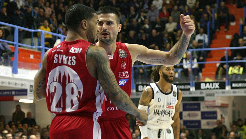 Due giocatori di basket vestiti di rosso con la tuta dell'Olimpia, parlano in campo