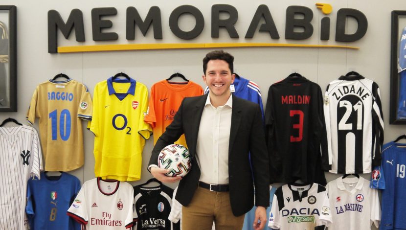 Alberto Zaccheti Ciriani con in mano un pallone da calcio, sullo sfondo la scritta "Memorabid" in alto e sotto magliette di calciatori appese