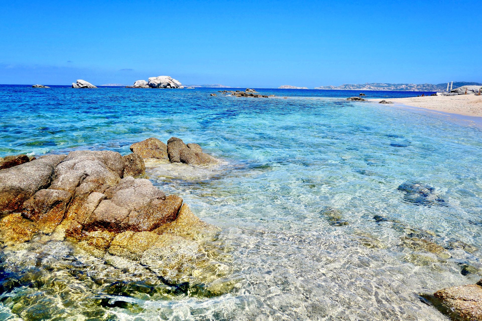 Mare molto azzurro e trasparente, a destra ci sono due scogli, sullo sfondo una barca