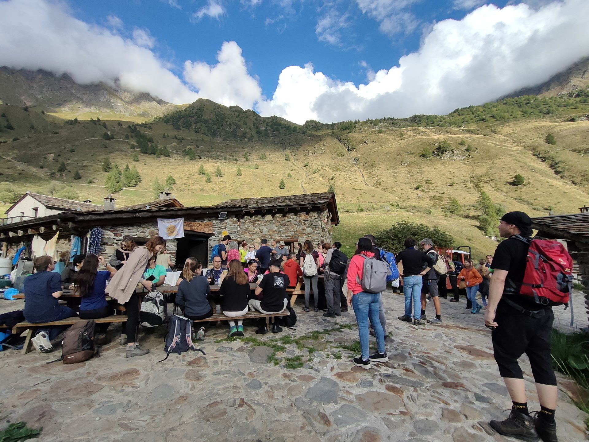 Un gruppo di persone fuori da un edificio in pietra in montagna, sullo sfondo montagne verdi 