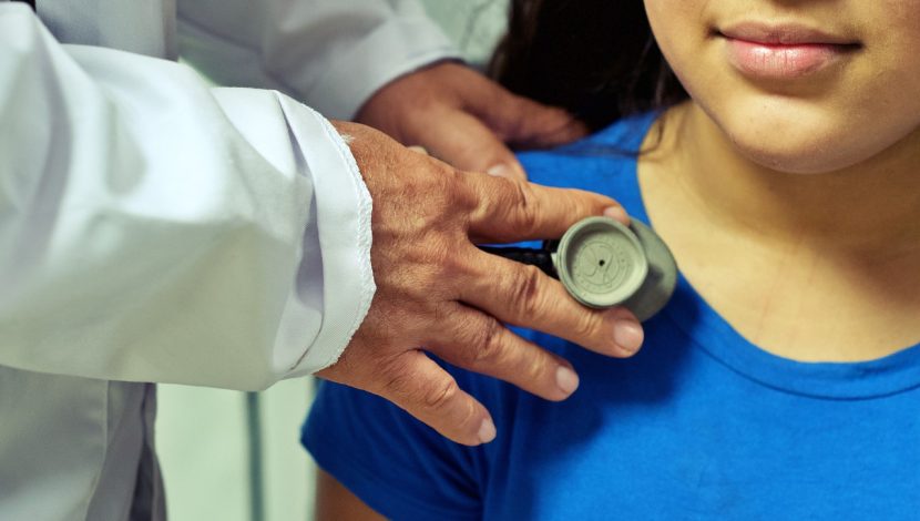 Il particolare della spalla di una bambina, a cui le mani di un medico appoggiano uno stetoscopio