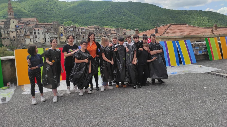 Un gruppo di ragazzi in posa fuori da una città, con dietro dei pannelli colorati