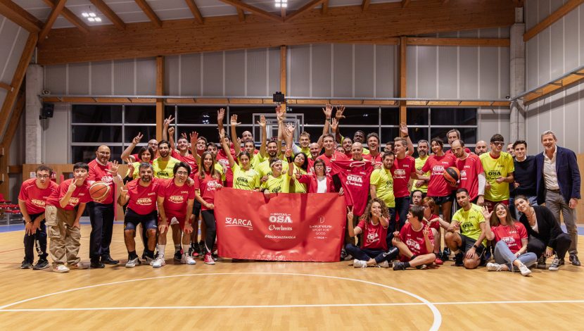 Un gruppo numeroso di ragazzi in una palestra, con magliette gialle e blu, in posa dietro a una bandiera rossa