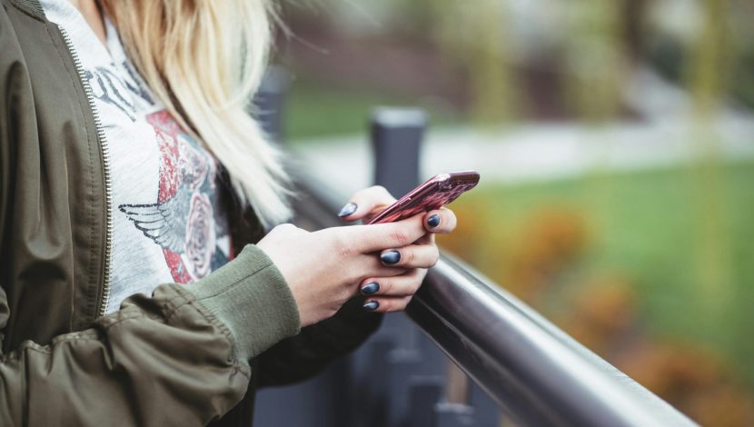 Immagine del busto di una donna bionda con in mano un telefono