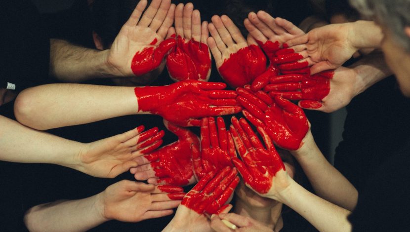 Tante mani vicine, che unite formano un cuore disegnato sui palmi con la vernice rossa