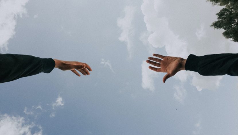 Due mani che si tendono l'una verso l'altra con sullo sfondo un cielo sereno con poche nuvole