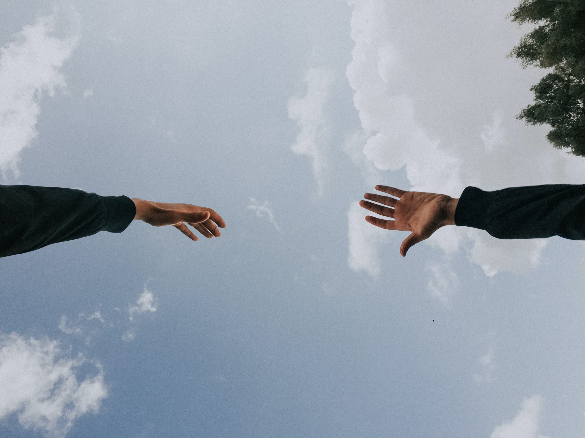 Due mani che si tendono l'una verso l'altra con sullo sfondo un cielo sereno con poche nuvole