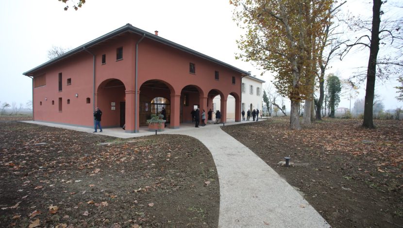 Un edificio rosso con un porticato circondato da un prato. Per arrivarci c'è una strada sterrata bianca