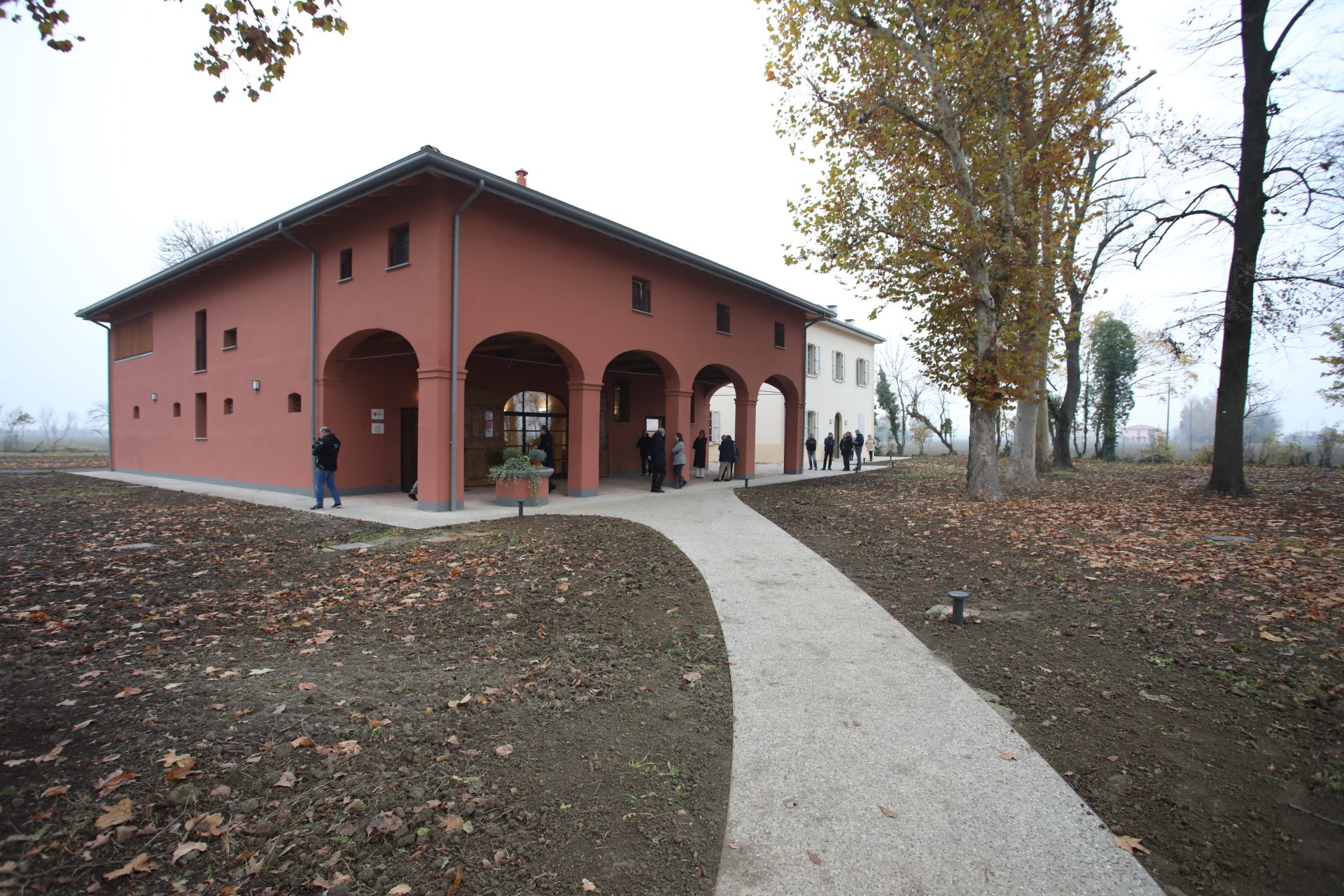 Un edificio rosso con un porticato circondato da un prato. Per arrivarci c'è una strada sterrata bianca