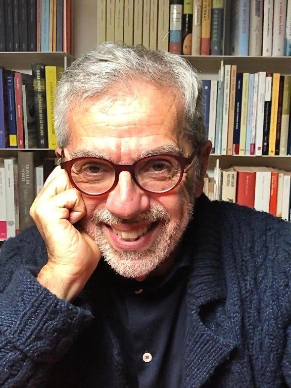 Giulio Lattanzi in primo piano, ha la barba corta, gli occhiali e i capelli grigi. Dietro una libreria 