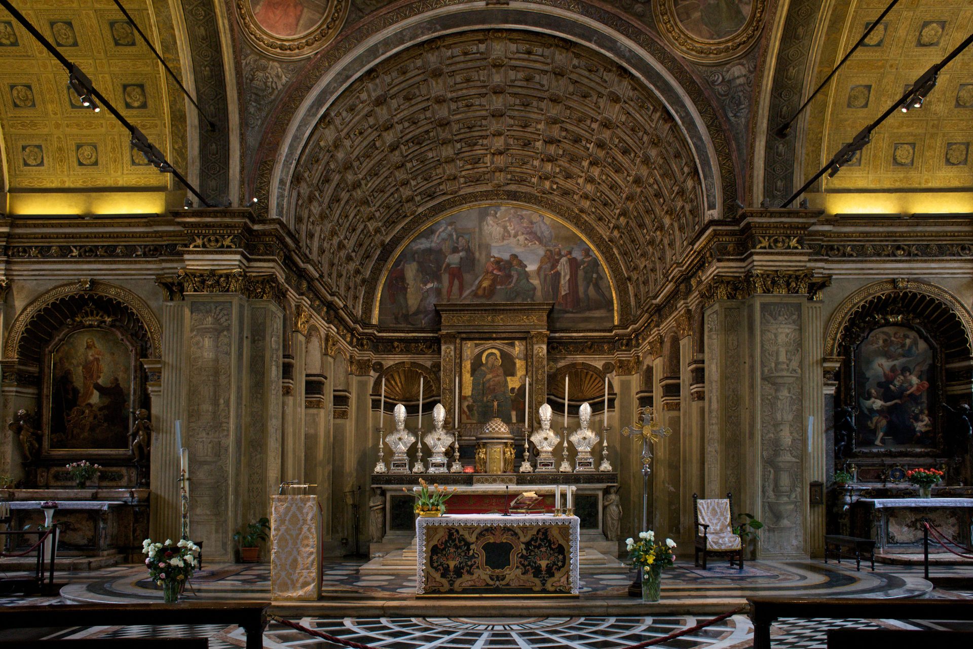 L'abside di una chiesa, con  un altare con 4 busti e delle candele 