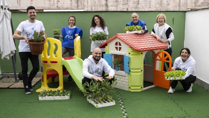 Alcune persone disposte dietro alcuni giochi per bambini (una casetta e uno scivolo), un uomo è seduto sullo scivolo