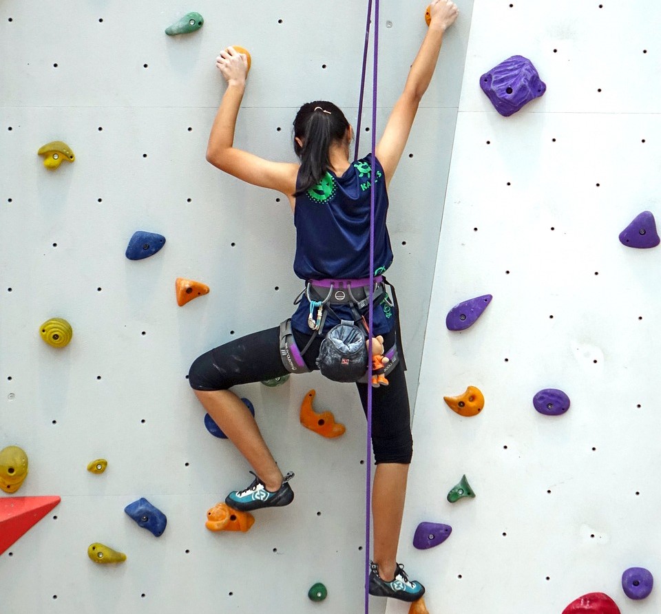 Una ragazzina che si arrampica su una parete di arrampicata indoor, con prese colorate e muro bianco