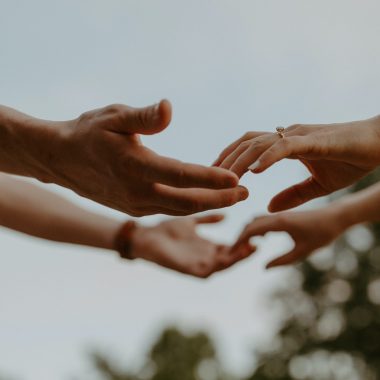Dettaglio delle mani di due persone, una di fronte all'altra all'aperto, mentre si stanno sfiorando