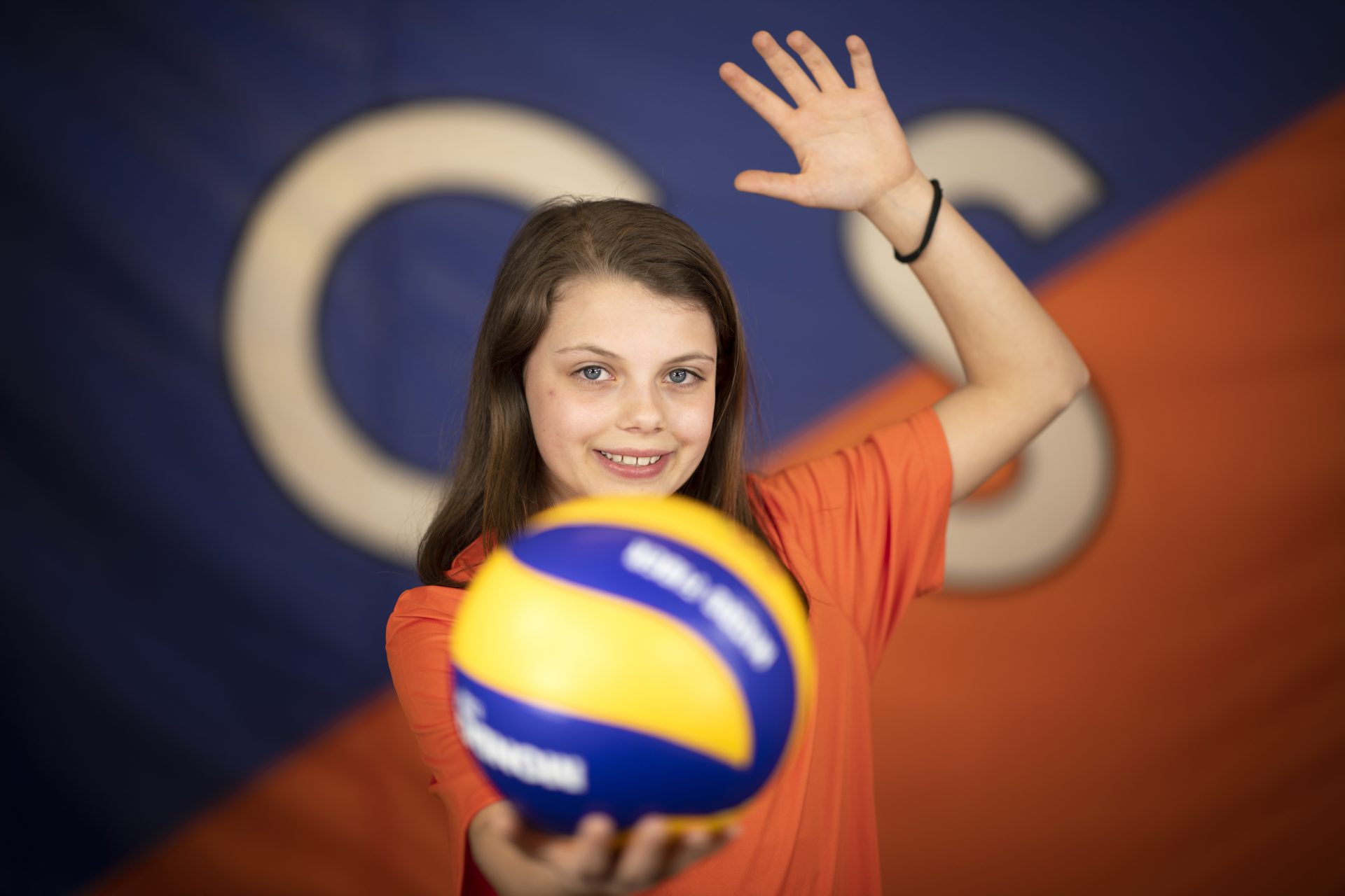 Una bambina con un pallone da pallavolo in mano e l'altro braccio alzato come a battere la palla 