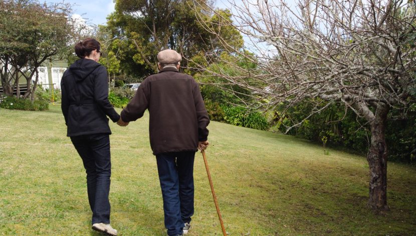 Una badante aiuta un anziano a camminare nel parco