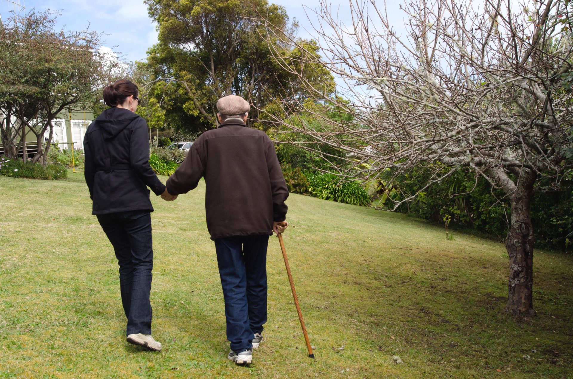Una badante aiuta un anziano a camminare nel parco