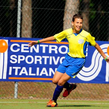 Un ragazzo che corre vestito da calcio, sullo sfondo un banner con scritto "Centro sportivo italiano"