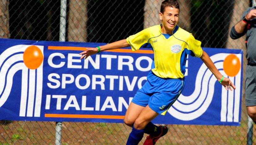 Un ragazzo che corre vestito da calcio, sullo sfondo un banner con scritto "Centro sportivo italiano"