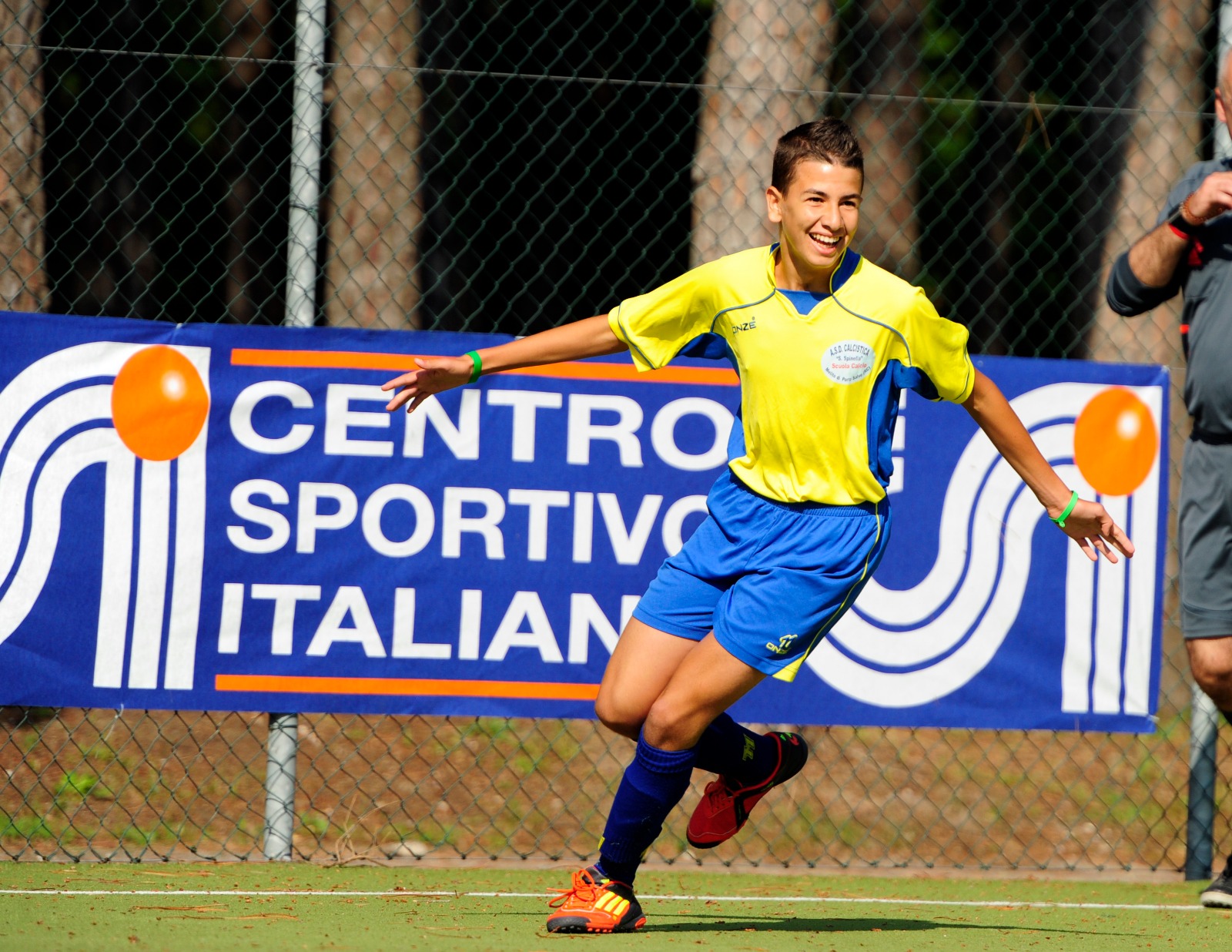 Un ragazzo che corre vestito da calcio, sullo sfondo un banner con scritto "Centro sportivo italiano"
