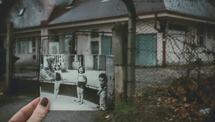 Vecchia foto di bambini davanti a una casa con le finestre sbarrate. Suggerisce idea di adozione e ricerca origini