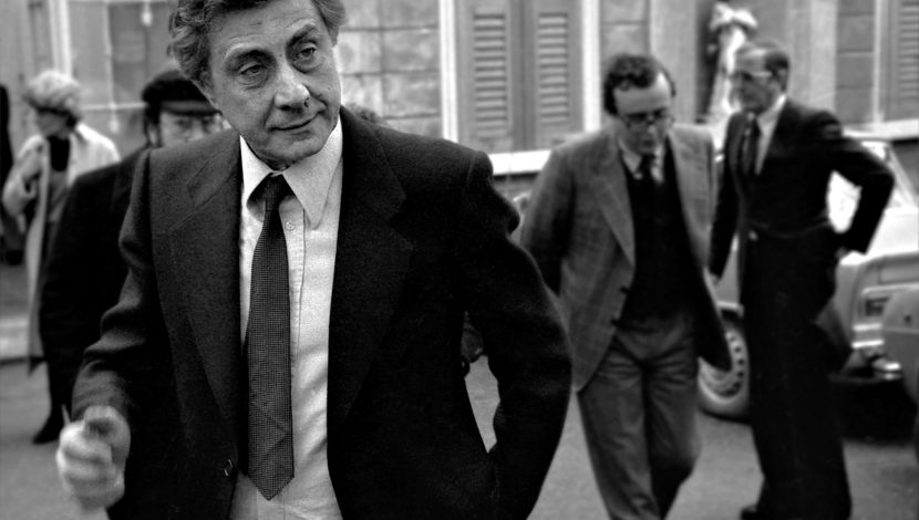 Foto in bianco e nero di Franco Basaglia in piano americano, che cammina, alle sue spalle altre figure
