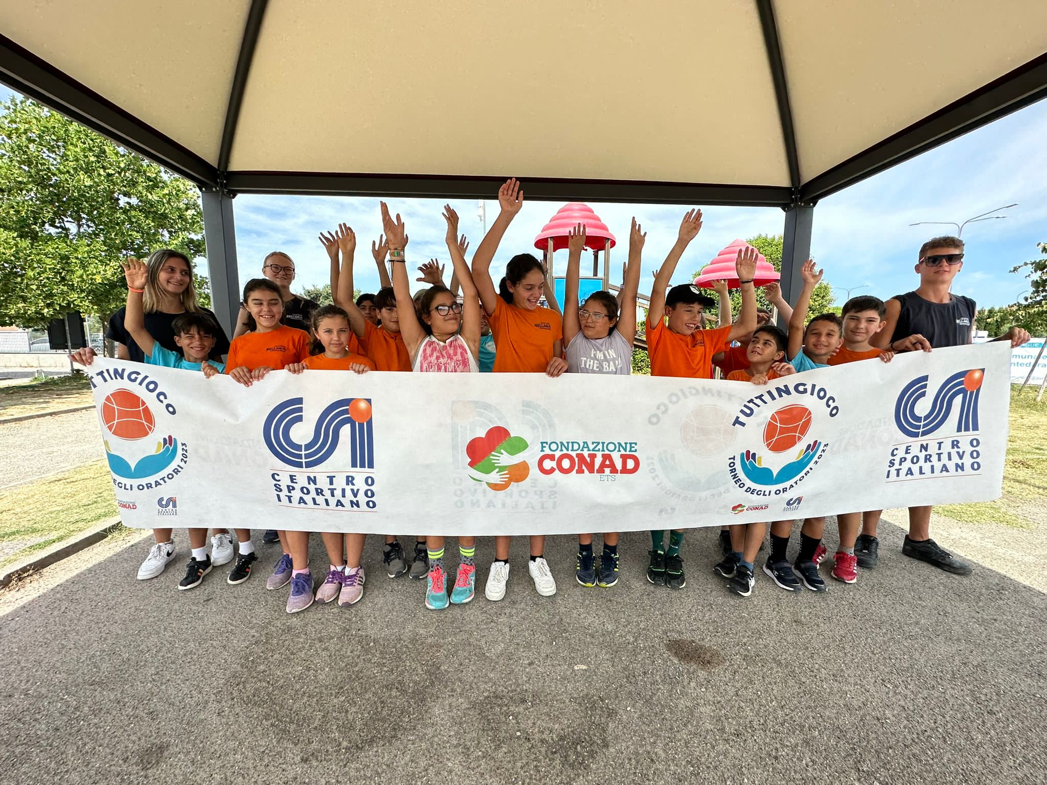 Dei bambini che alzano le mani tenendo uno striscione con i loghi di Tuttingioco, Csi e Fondazione Conas Ets