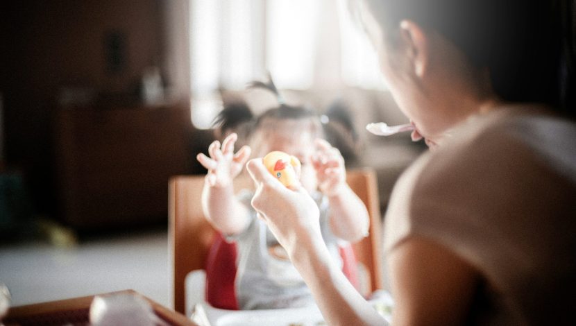 mamma che imbocca una bambina seduta nel seggiolone