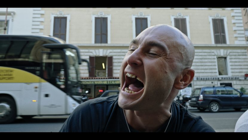 un primo piano di un uomo che urla, dietro a lui un palazzo