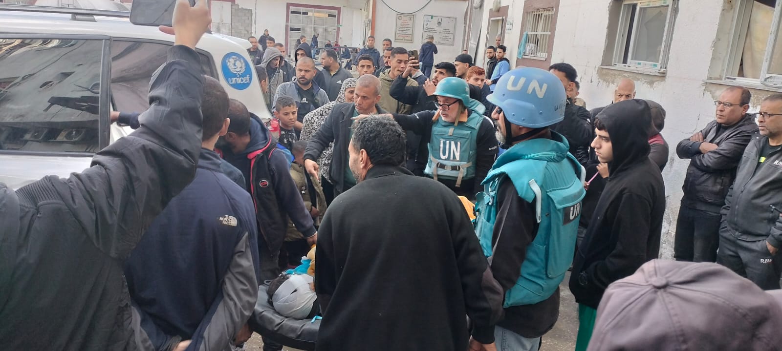 Folla di persone attorno a una barella, due hanno casco e gilet delle nazioni unite con scritto "Un"